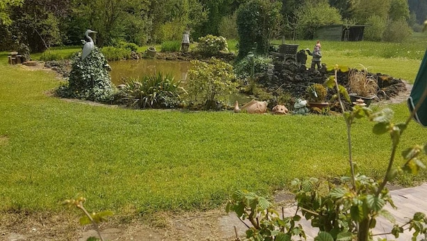 Un jardin paisible avec un étang, une végétation luxuriante et une statue d’oiseau.