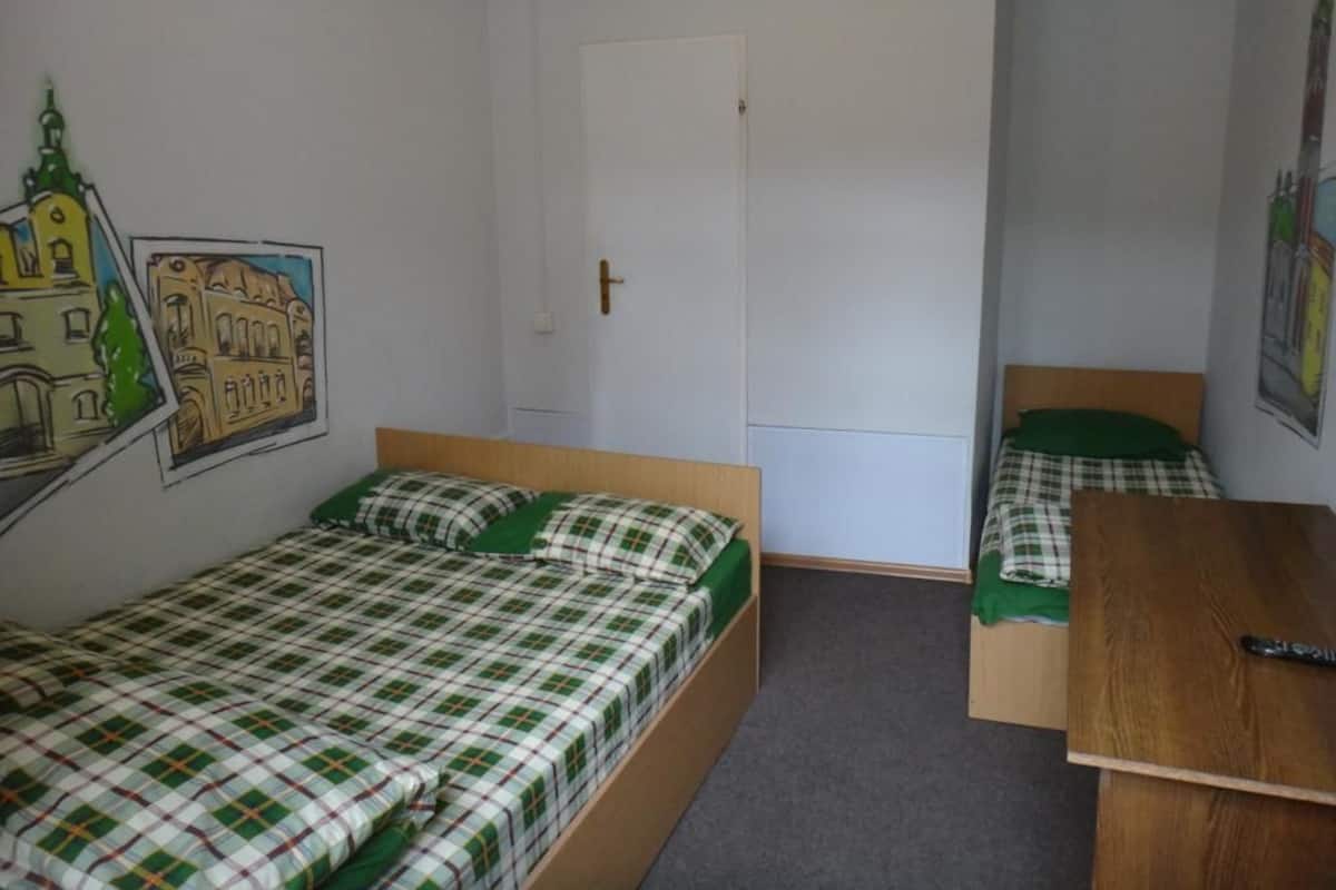 A small, simple room with two single beds, a wooden desk, and a door.