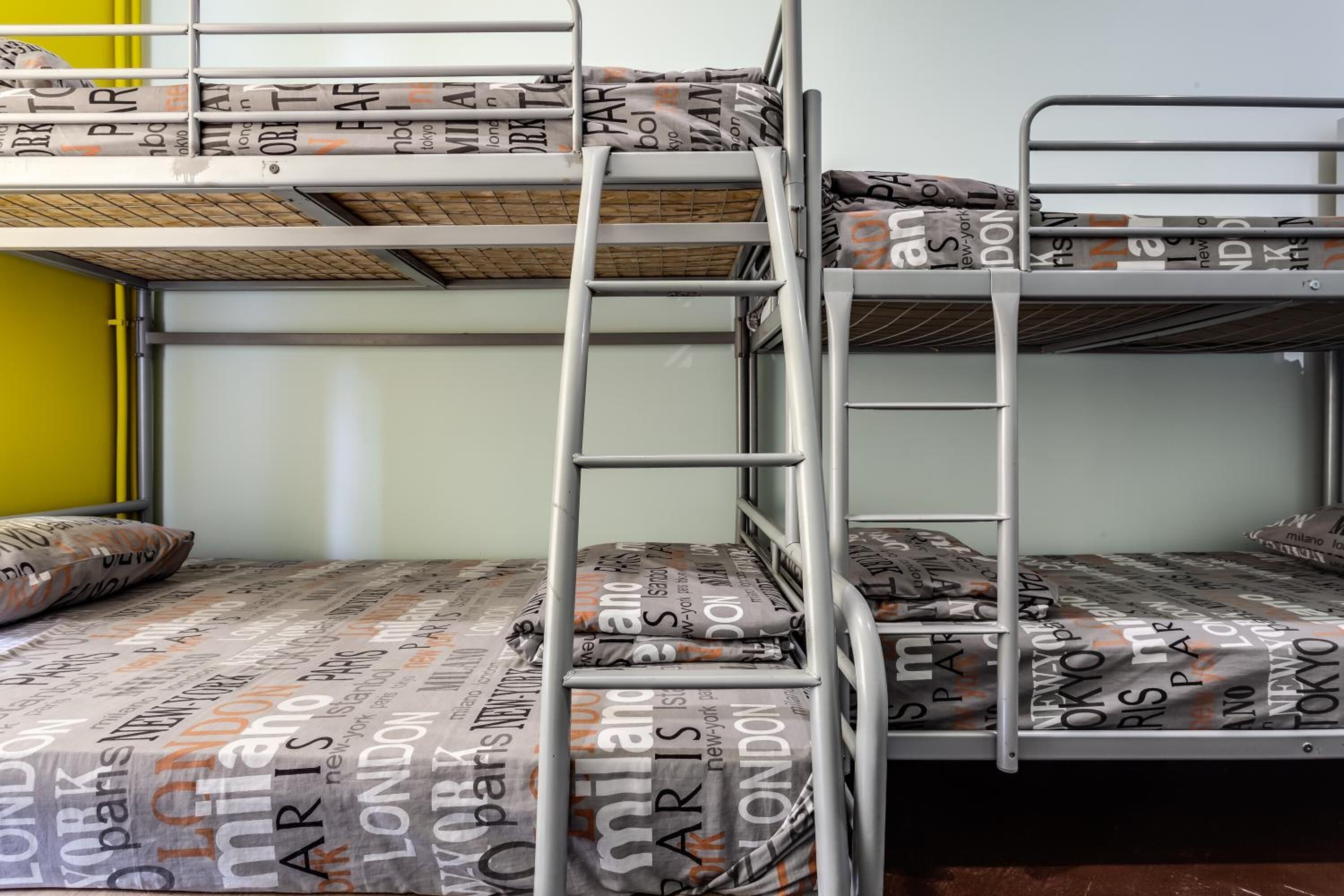 A bunk bed with metal railings and a ladder, featuring a patterned mattress with city names.