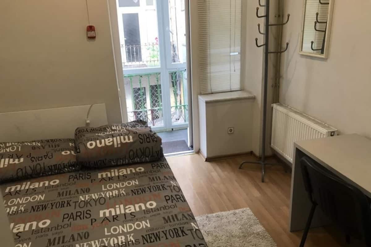 A room with a bed, a desk, a radiator, and a window with blinds.
