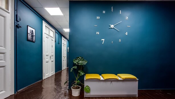 A hallway with a blue wall, a large clock, and a bench with yellow cushions. - Mister Econom Hotel - Hostel (Lviv)