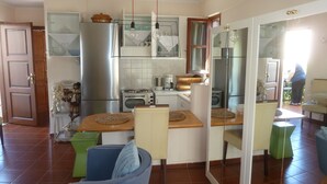 A compact kitchen with a refrigerator, oven, and microwave. There are two chairs and a small dining table. - Calergi 15: Boutique Resort 1BDR/1LVR Apt- Pool/Rooftop/Nature/Sunset/Rethymno (Ατσιπόπουλο)