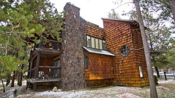 A rustic cabin with a stone chimney, wooden exterior, and a balcony.