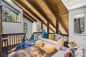A spacious balcony with a wooden ceiling, a white sofa with cushions, a leather rug, and a small table with a plant.