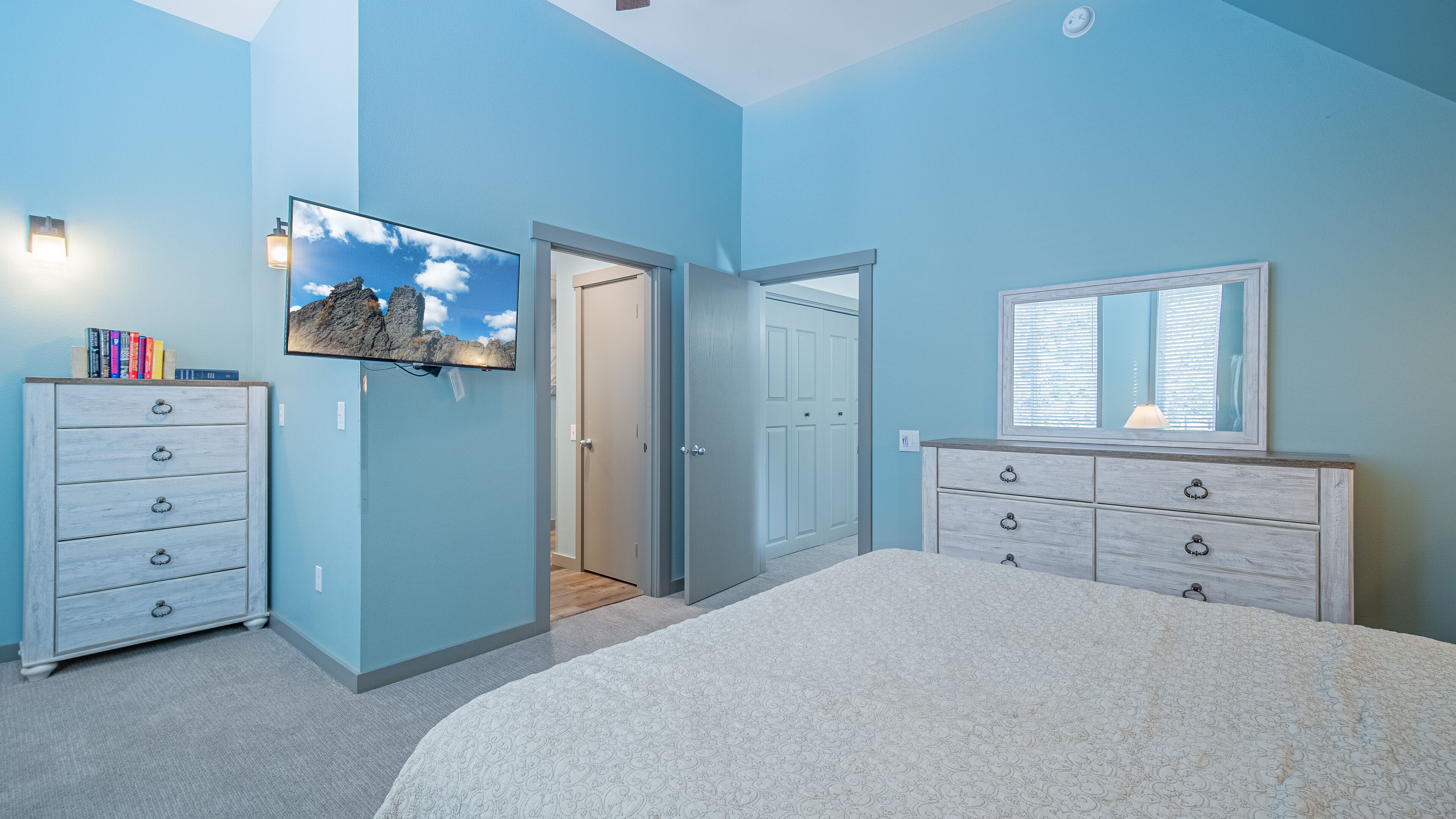 Une chambre à coucher comprenant un lit, deux commodes, un téléviseur et une porte donnant sur une autre pièce.