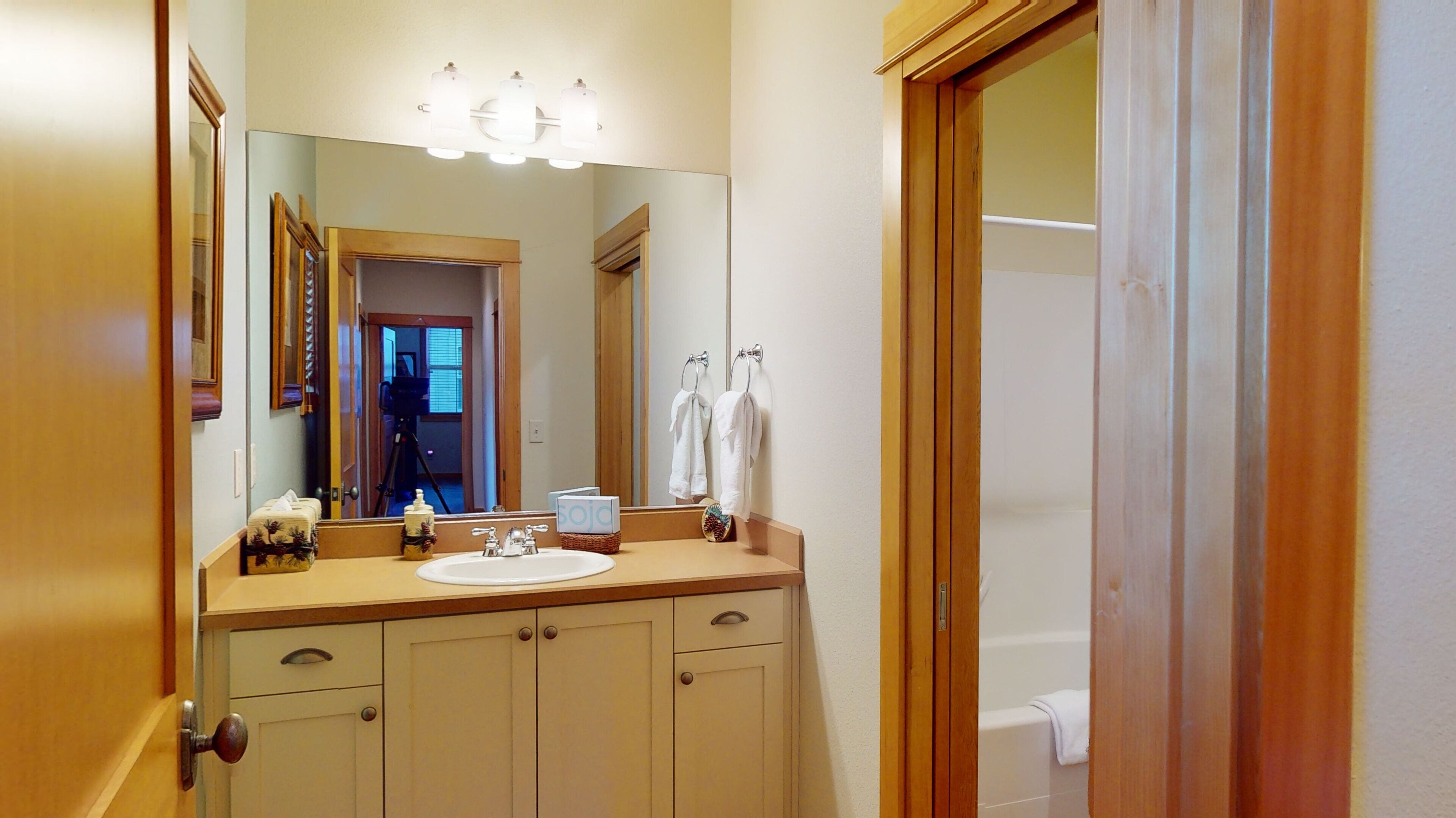 A bathroom with a wooden vanity, a large mirror, and a bathtub.