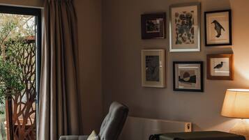 A hotel room with a bed, a chair, a table, a suitcase, and a wall with framed pictures.