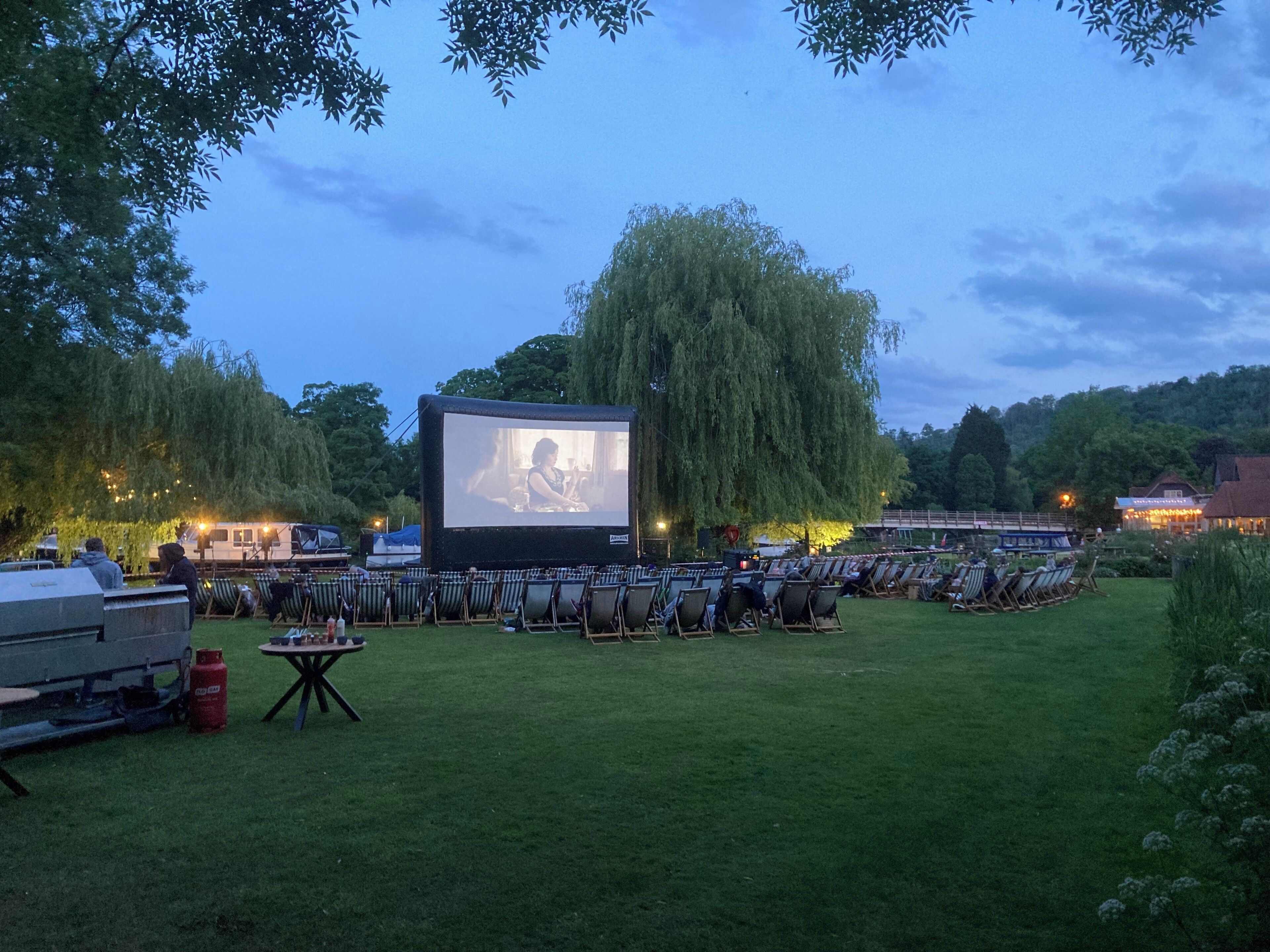 Un cinéma en plein air doté d’un grand écran, de rangées de chaises de jardin et d’une pelouse.