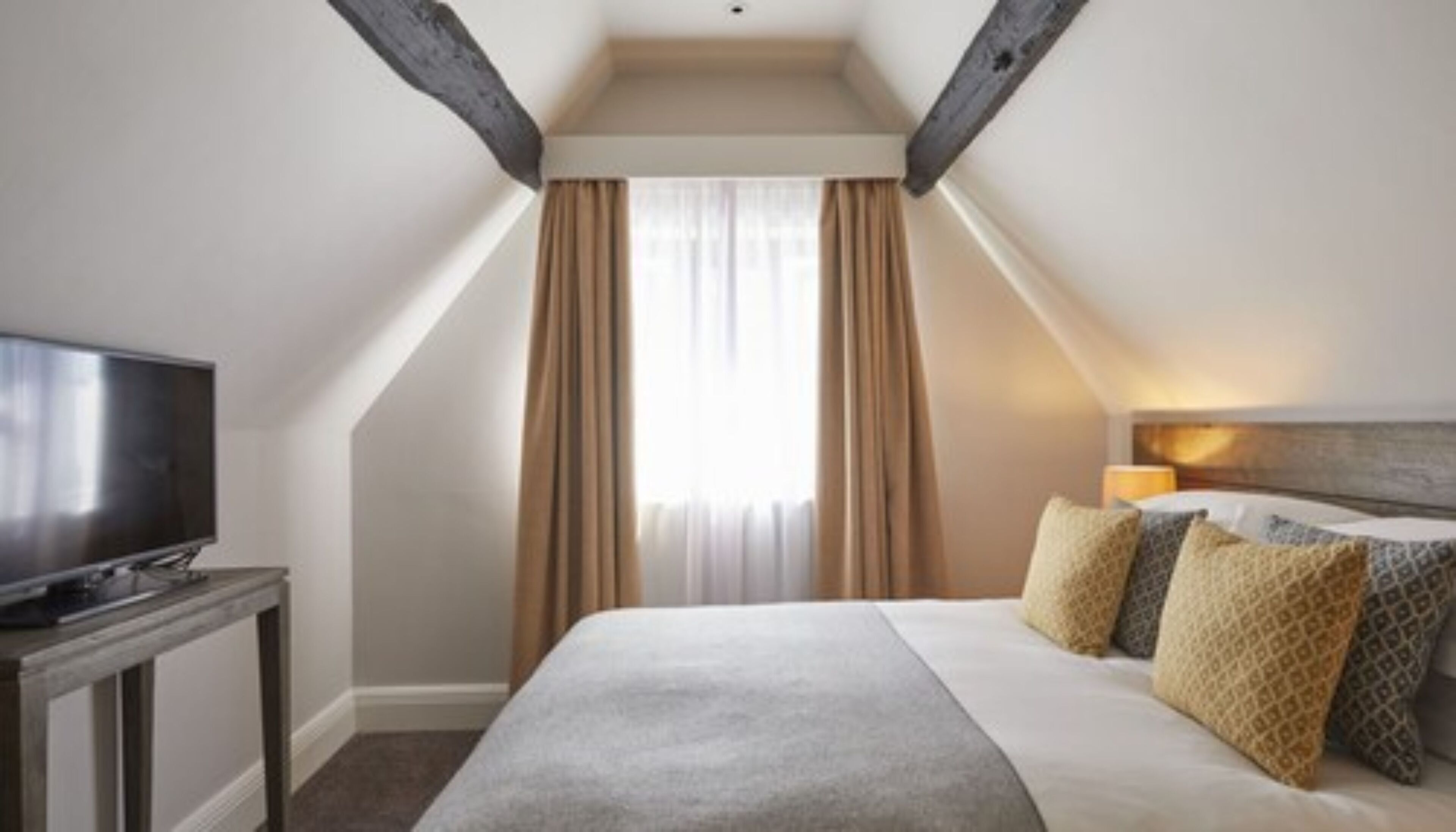 A hotel room with a large bed, a television on a stand, and a window with curtains.