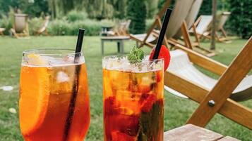 Dos bebidas sobre una mesa de madera al aire libre, con sillas y follaje de fondo.