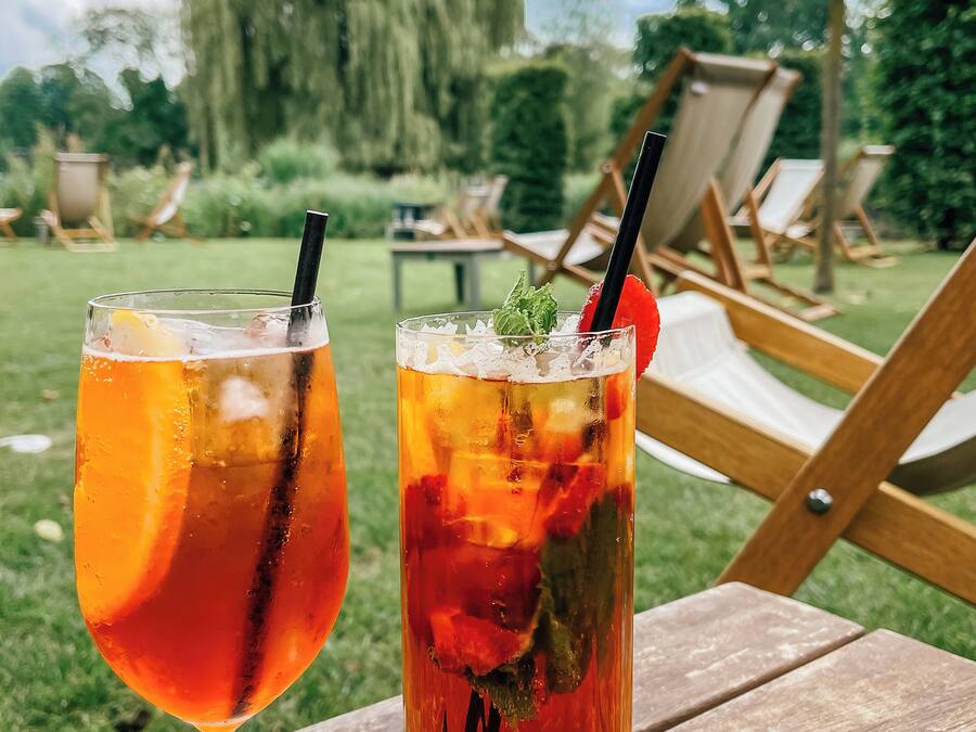 Dos bebidas sobre una mesa de madera al aire libre, con sillas y follaje de fondo.