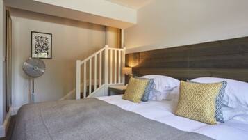 A hotel room with a bed, a headboard, a staircase, and a wall-mounted fan.