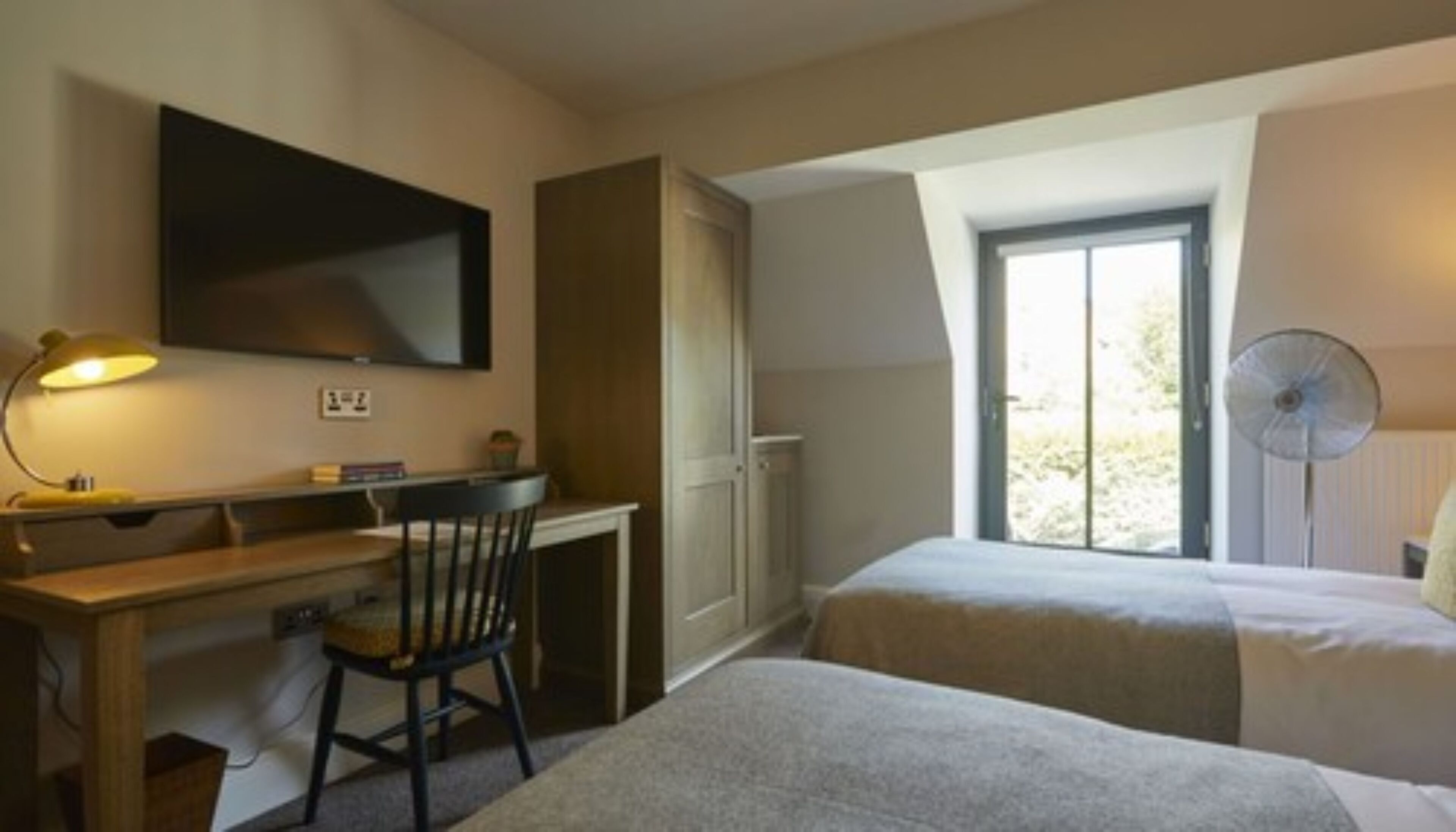 Habitación de hotel con escritorio, silla, dos camas, televisor y ventana con vistas.