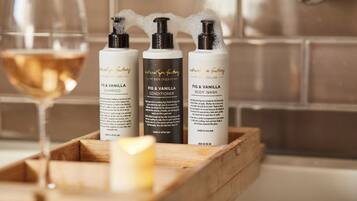Three bottles of Fig & Vanilla body wash, a glass of wine, and a candle on a wooden tray.