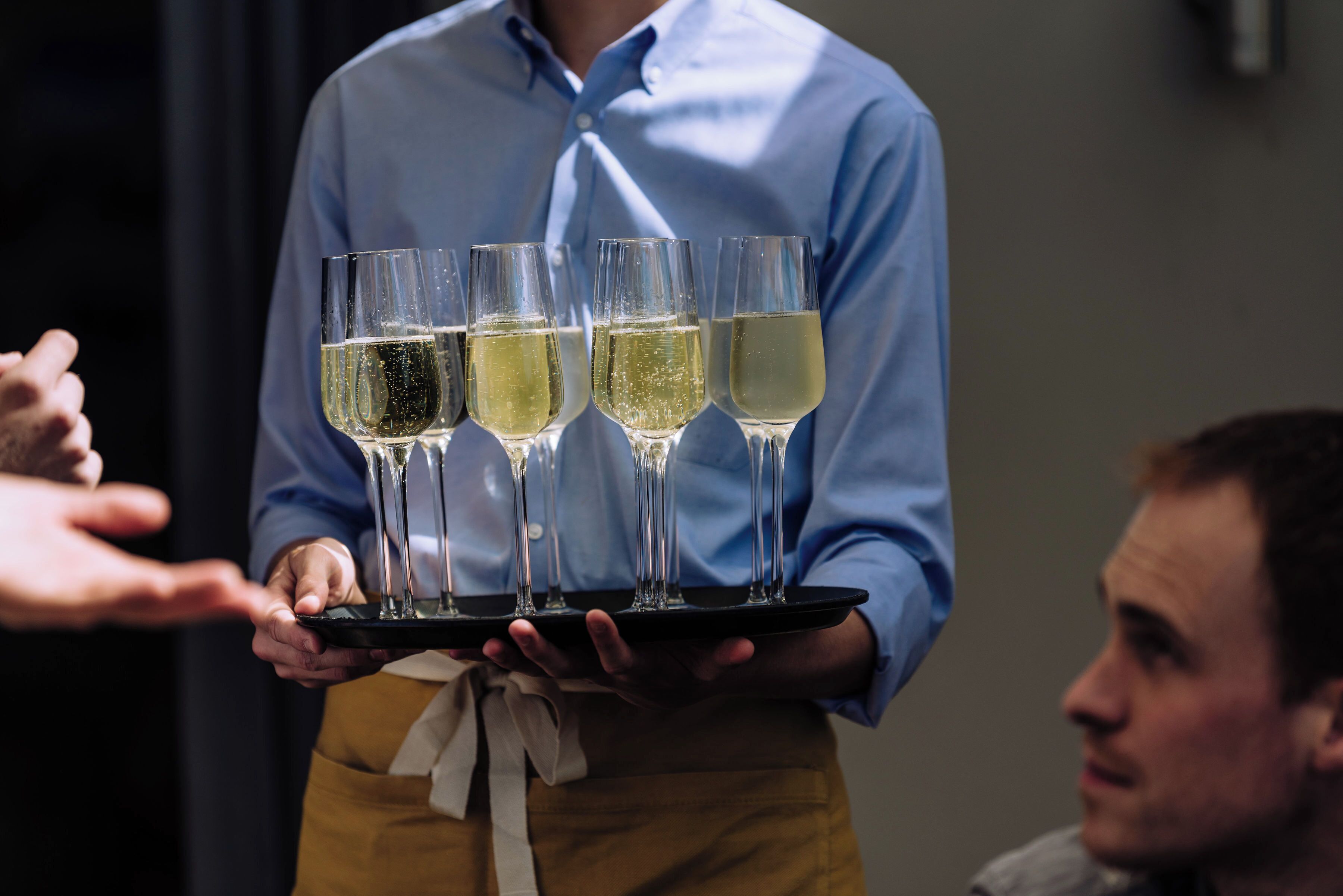 A person holding a tray with four glasses of white wine.