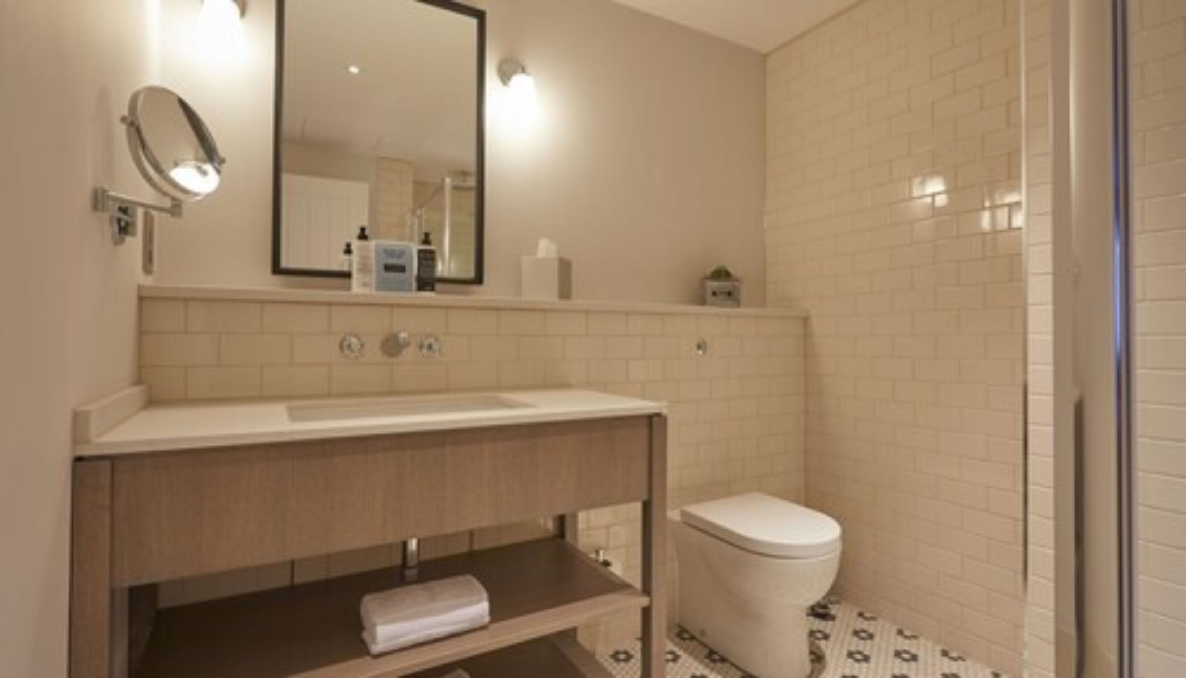 A bathroom with a white sink, mirror, and toilet. There is a towel on the shelf and a small plant on the counter.