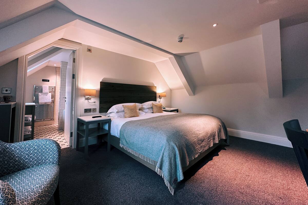 A bedroom with a bed, bedside tables, a chair, and a bathroom visible through an open door.