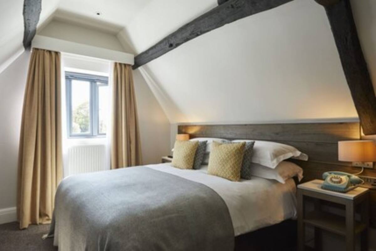 A bedroom with a large bed, a nightstand, a lamp, and a window with curtains.