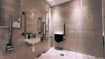 Un baño moderno con lavamanos, barras de apoyo, ducha y toallero.