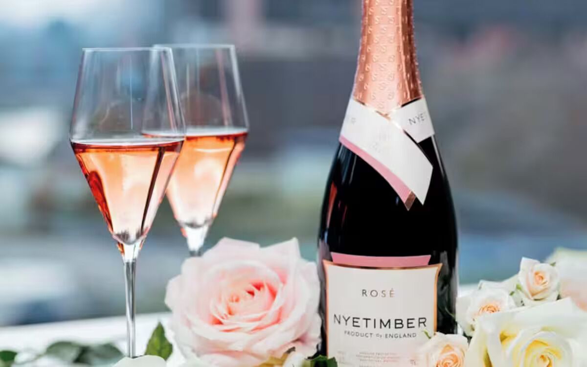 Una botella de vino Nyetimber con dos copas de vino rosado y rosas.
