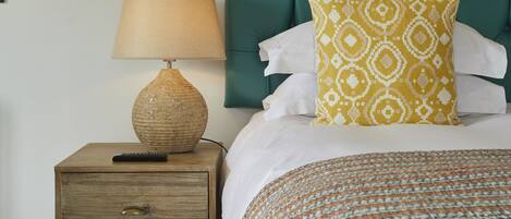 Un lit bien fait, agrémenté d’un coussin à motifs, d’une lampe de chevet et d’une table de nuit en bois.