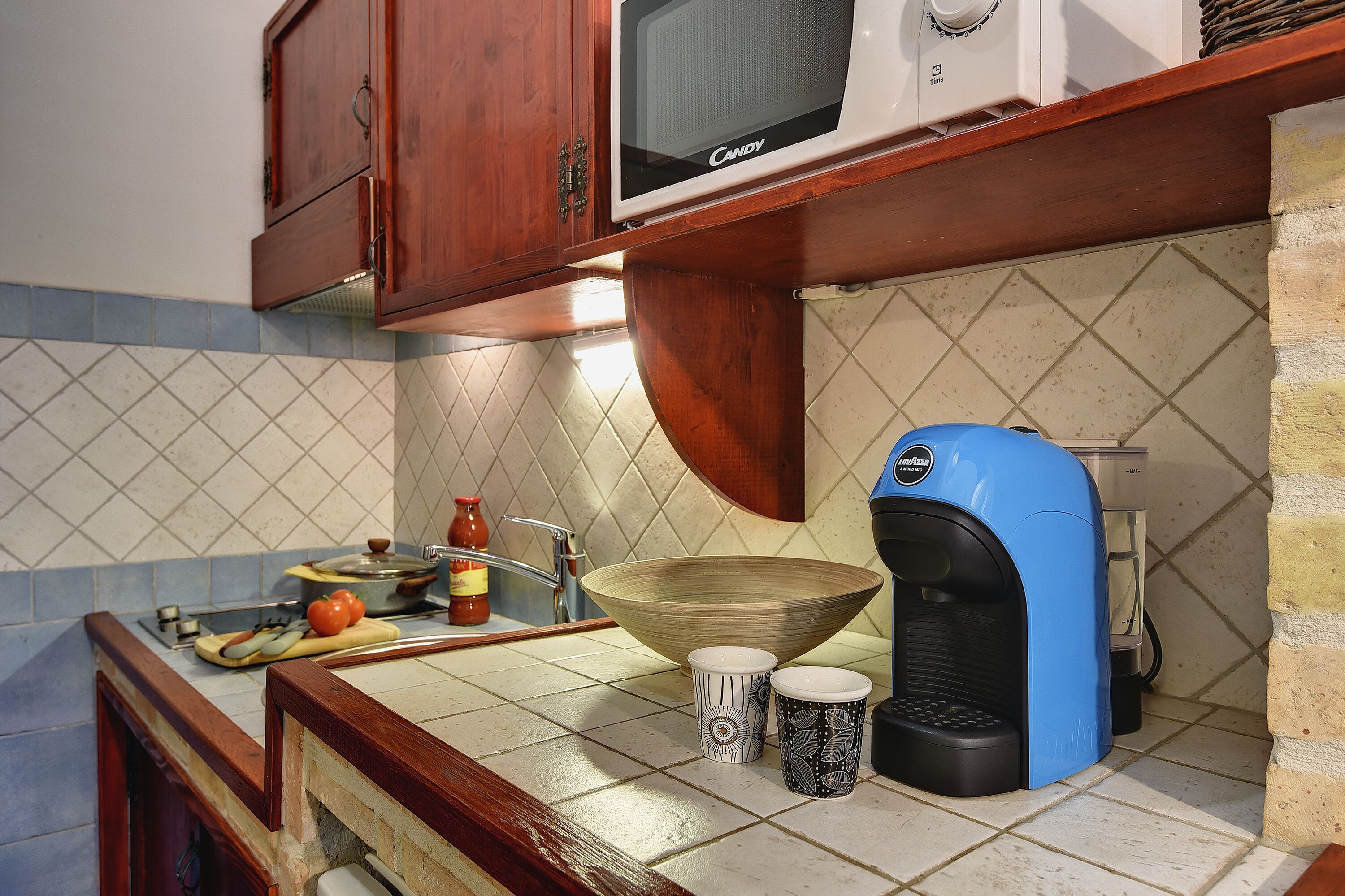 Una cucina con mobili in legno, un forno a microonde, una macchina da caffè e una ciotola grande sul ripiano.
