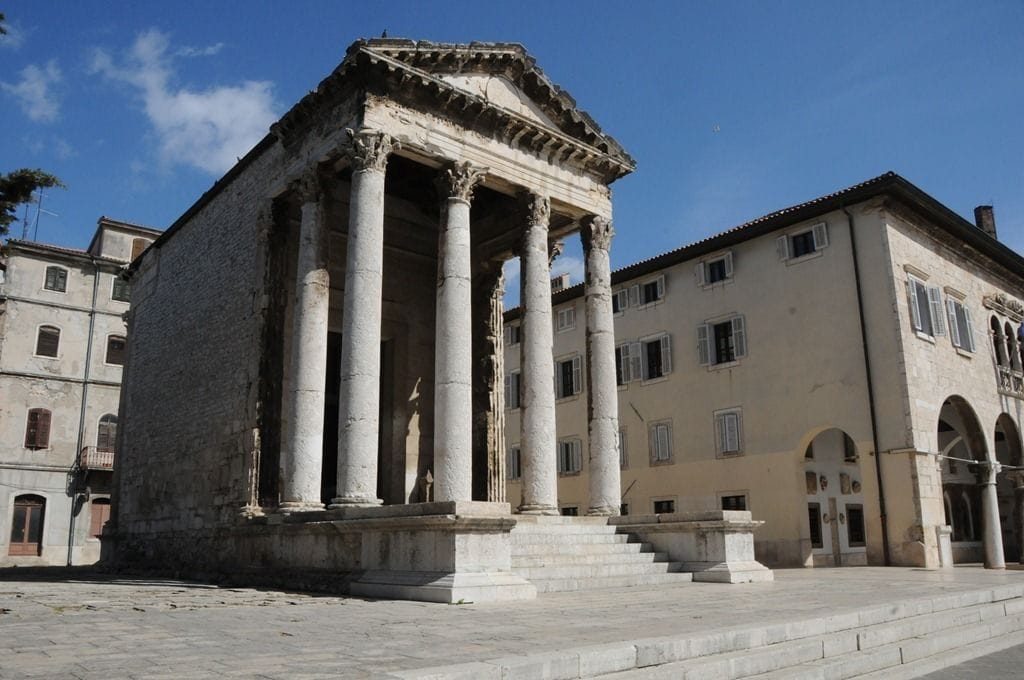 A classical building with columns and a pediment, surrounded by other buildings.