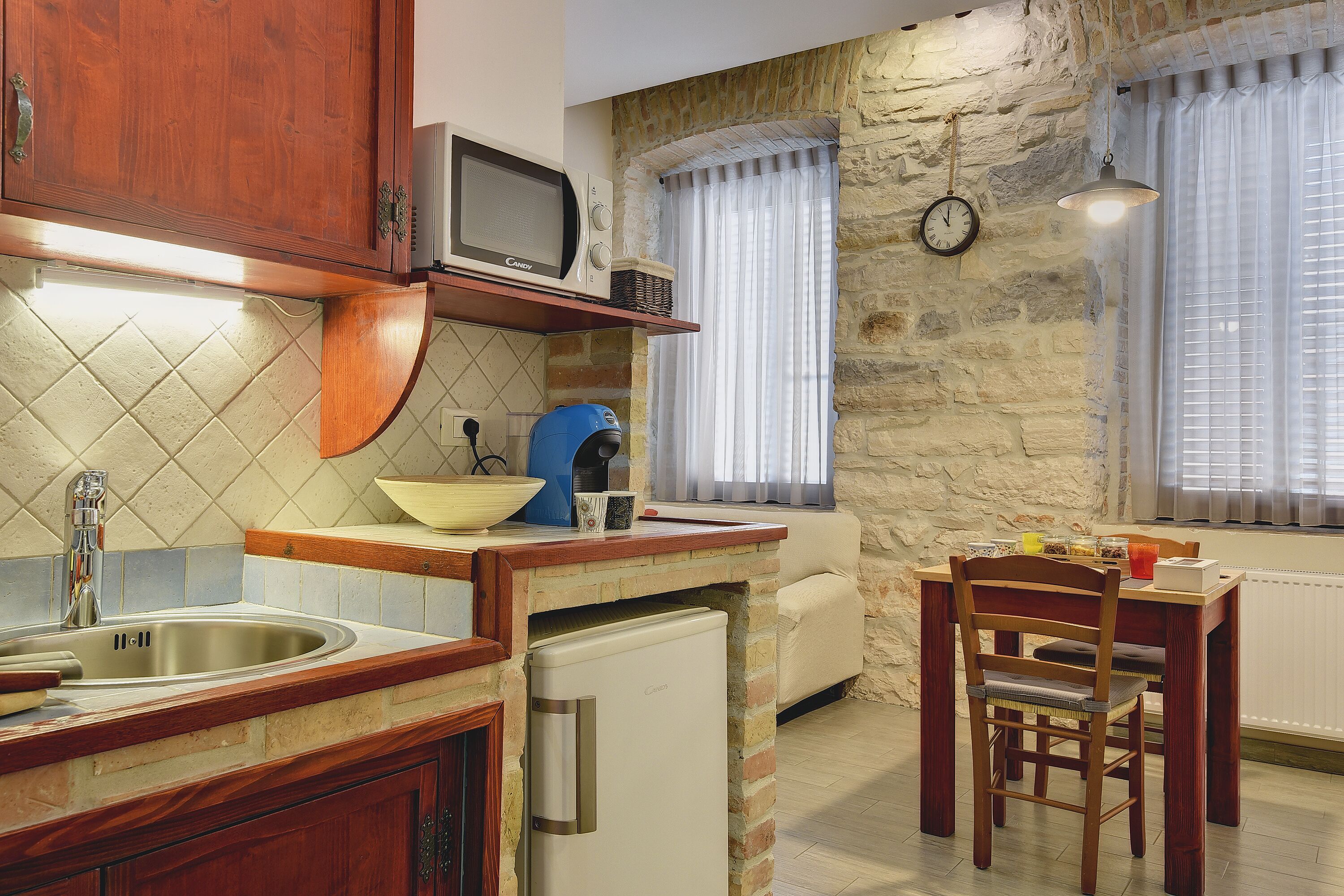 A kitchen with a built-in microwave, a sink, and a refrigerator. There is a dining table with chairs and a window with curtains.