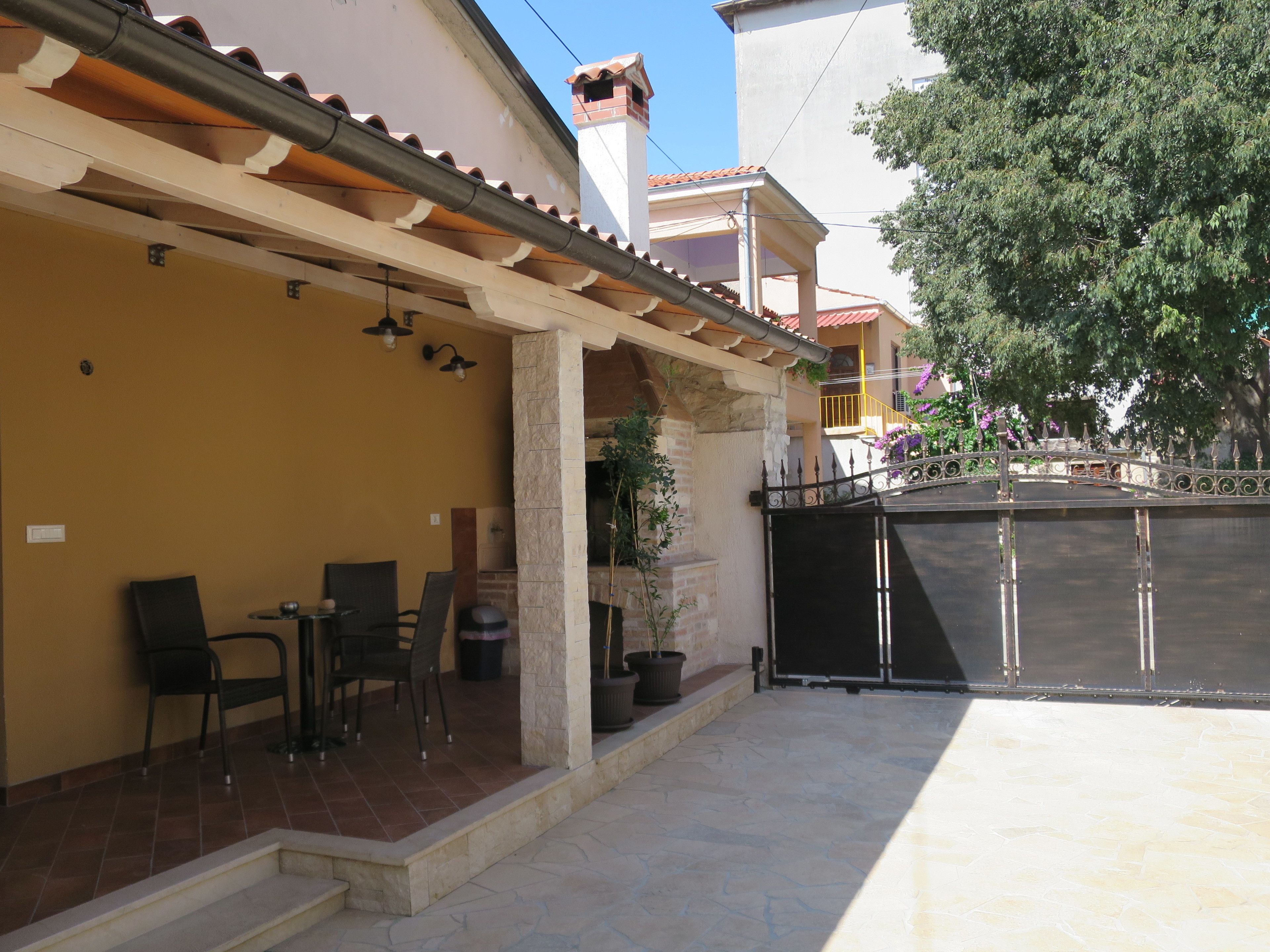 A covered patio area with outdoor seating, a stone pillar, and a gated entrance.