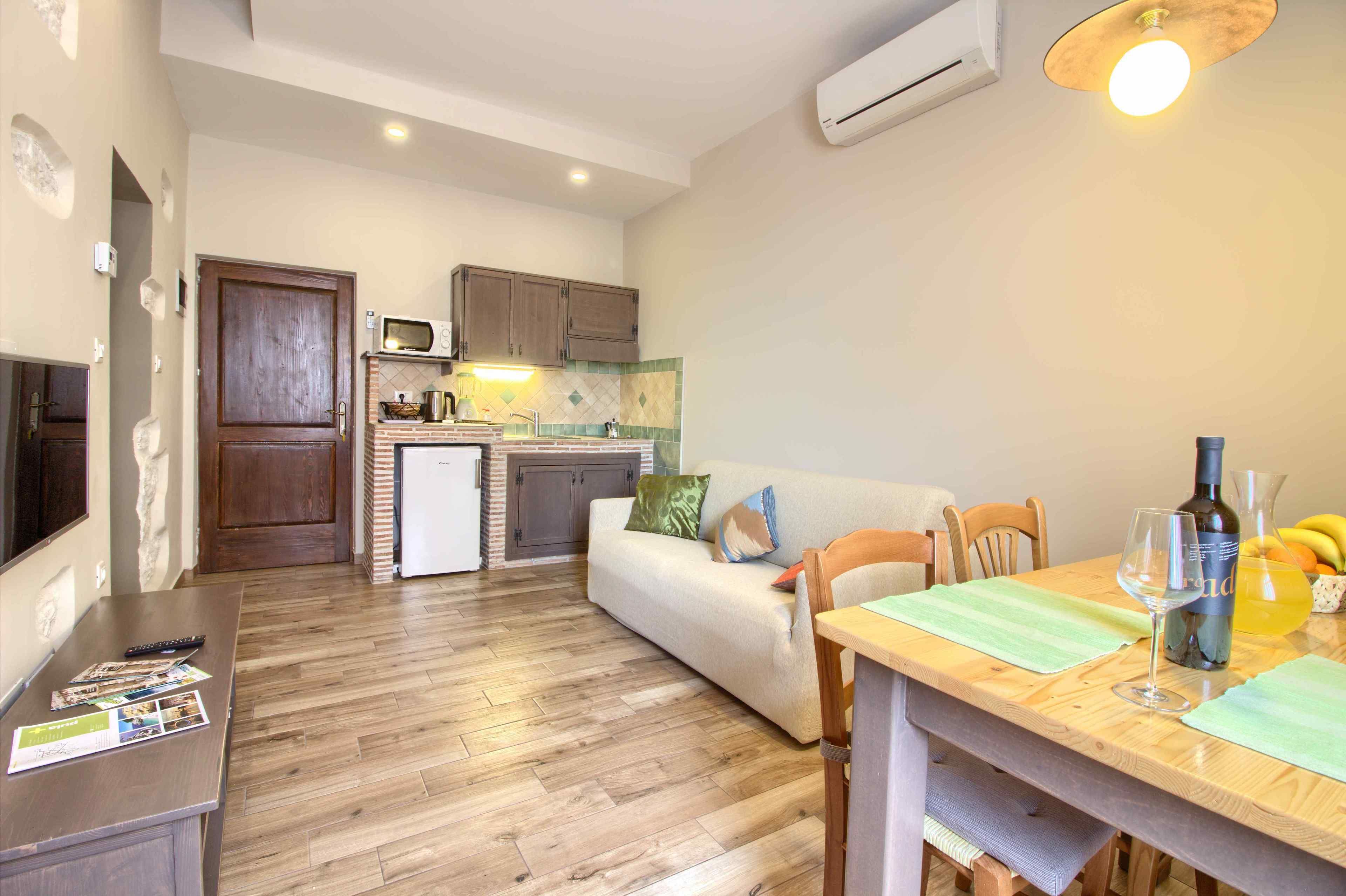 A compact kitchen with a microwave, sink, and a small refrigerator. There is a wooden dining table with a glass and a bottle on it.