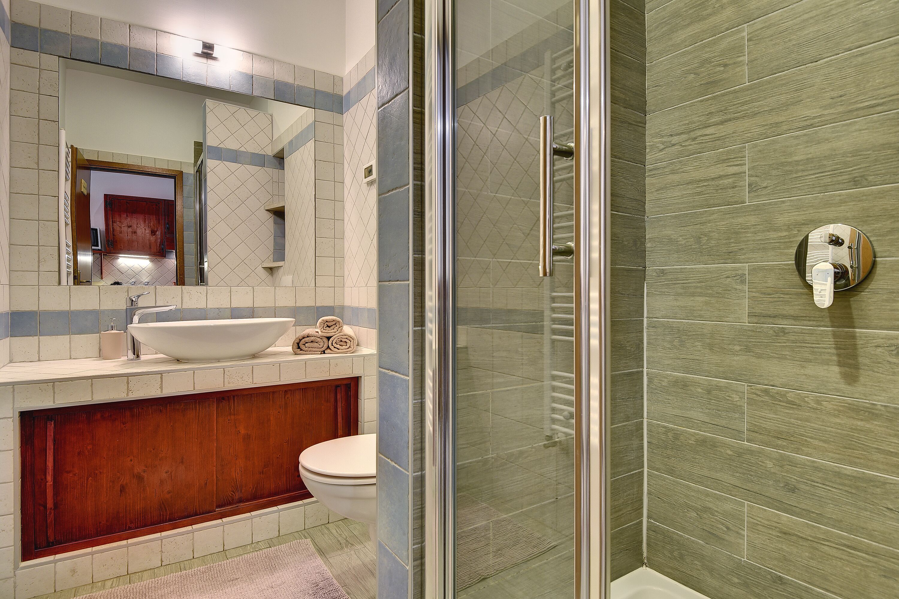 A modern bathroom with a glass shower enclosure, a wooden vanity, and a large mirror above the sink.