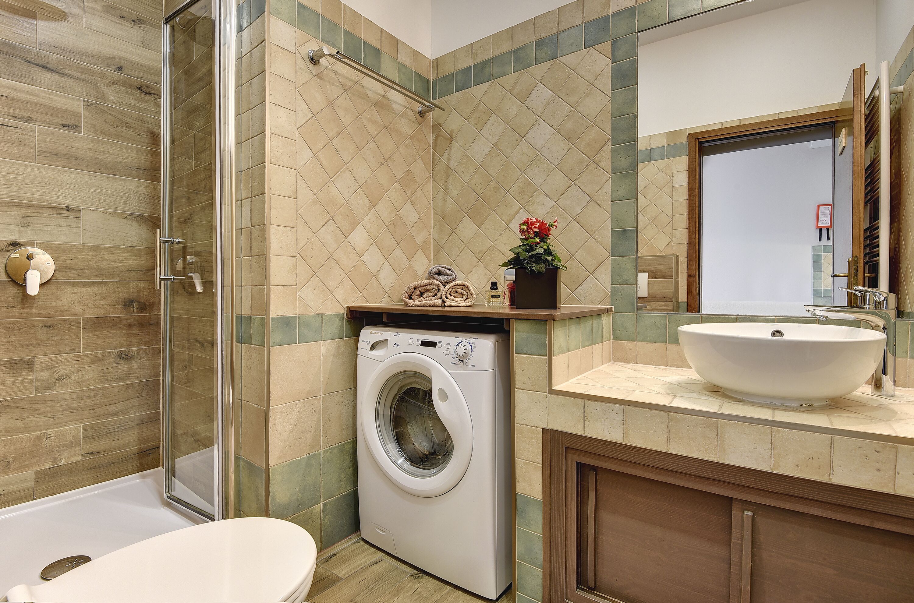Un baño moderno con ducha envuelta en vidrio, lavadora integrada, lavamanos y retrete.