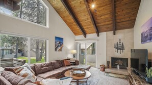 A spacious living room with a large sectional sofa, a fireplace, a television, and large windows offering views of the outdoors. - Tennis Village Escape with Access to Exclusive Golf (Bend)
