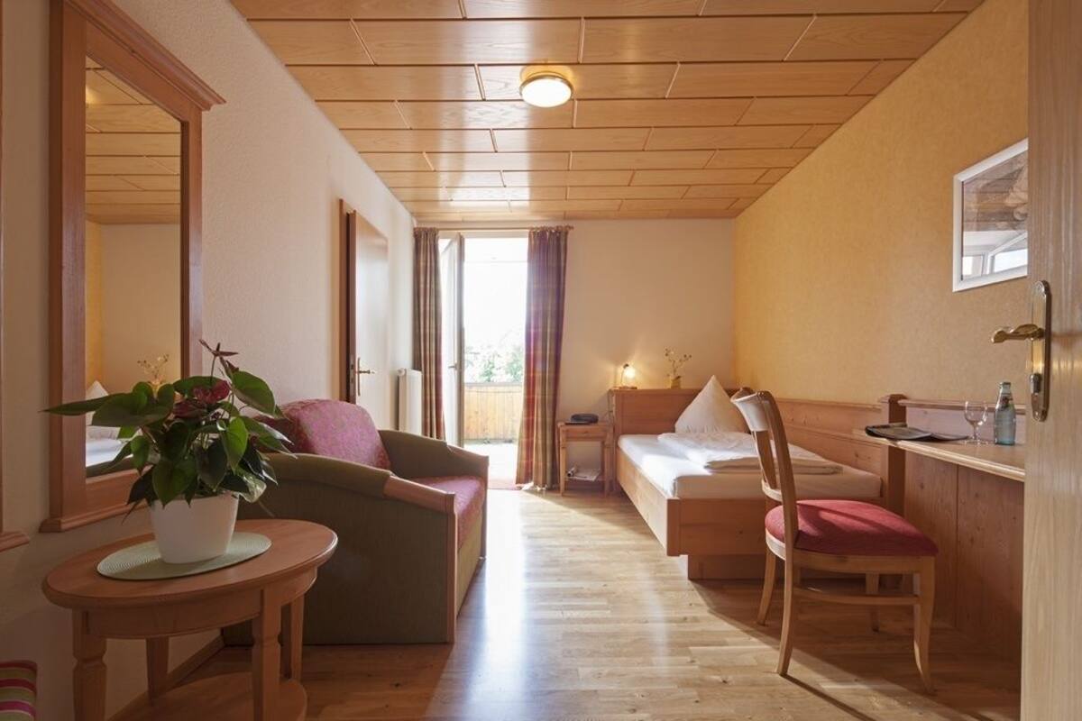 Una habitación acogedora con una cama, un sillón, una mesita con una planta y un espejo en la pared.