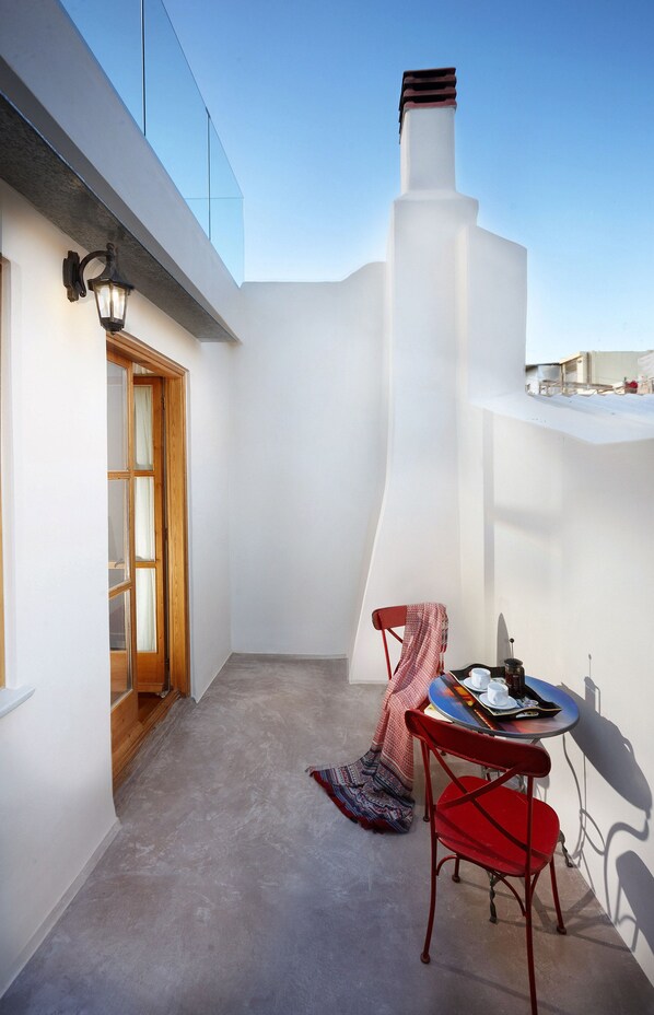 A small, enclosed balcony with a red chair, a table with a tray, and a white wall with a window. - Casa Perla Suites (Chania)