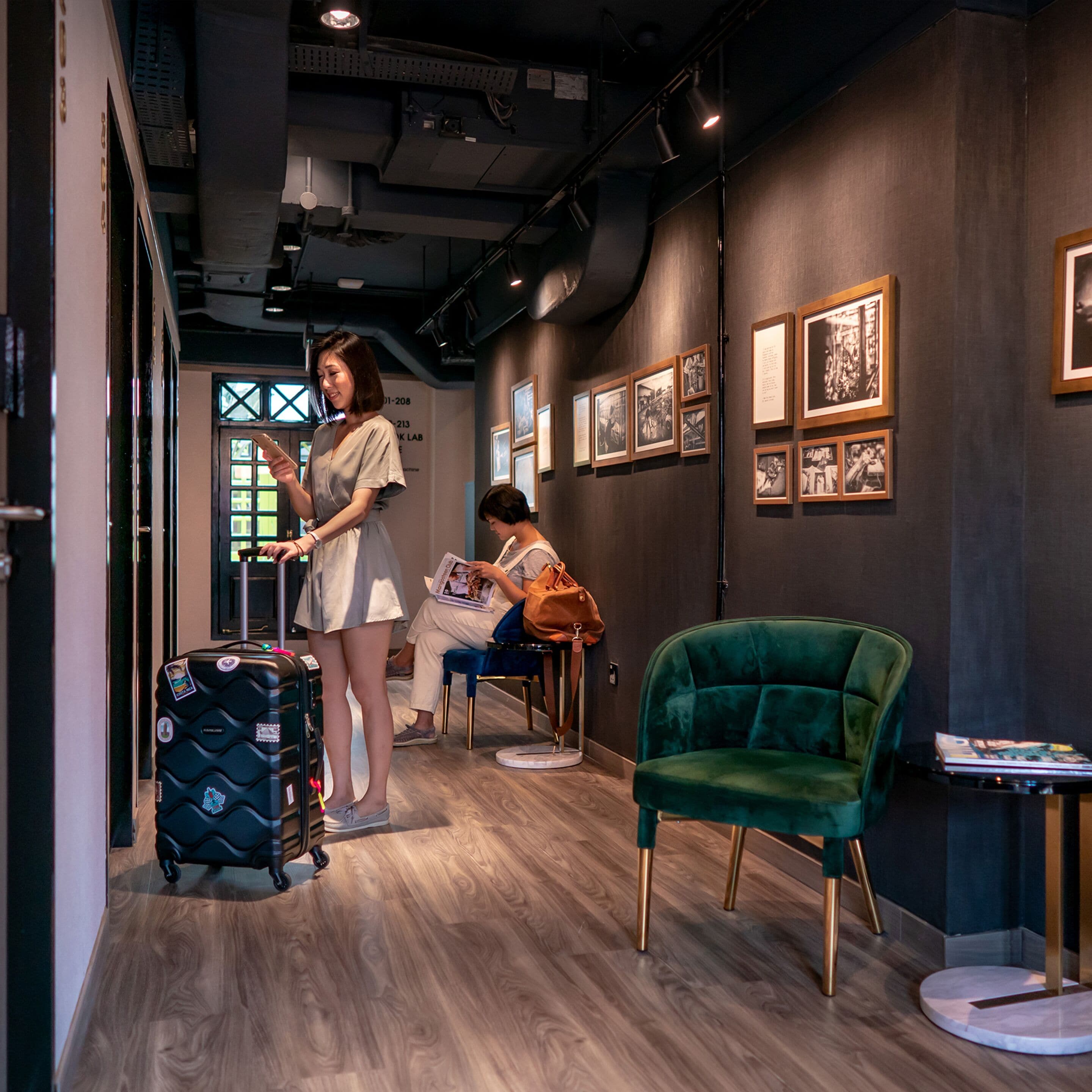 A modern interior with a wooden floor, a green velvet chair, and a wall with framed pictures.