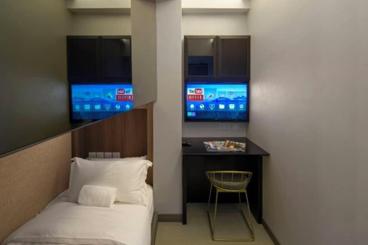 A small hotel room with a bed, a desk with a chair, and a TV displaying YouTube on the wall.
