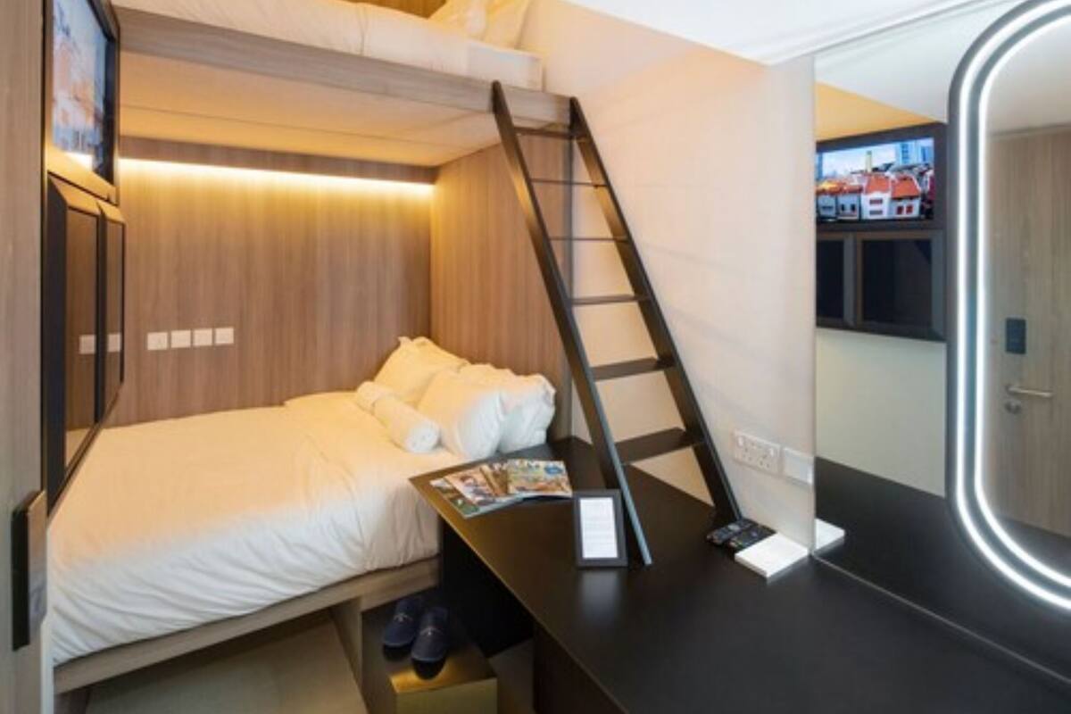 A compact bedroom with a bunk bed, a desk with a chair, a ladder, a large mirror, and a small storage drawer.