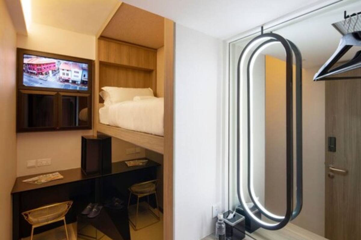 A compact hotel room with a bed, a desk, a chair, a TV, and a mirror.