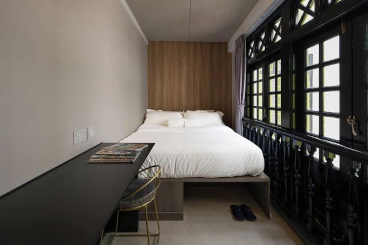 A bedroom with a bed, a desk, and a window with a black frame.