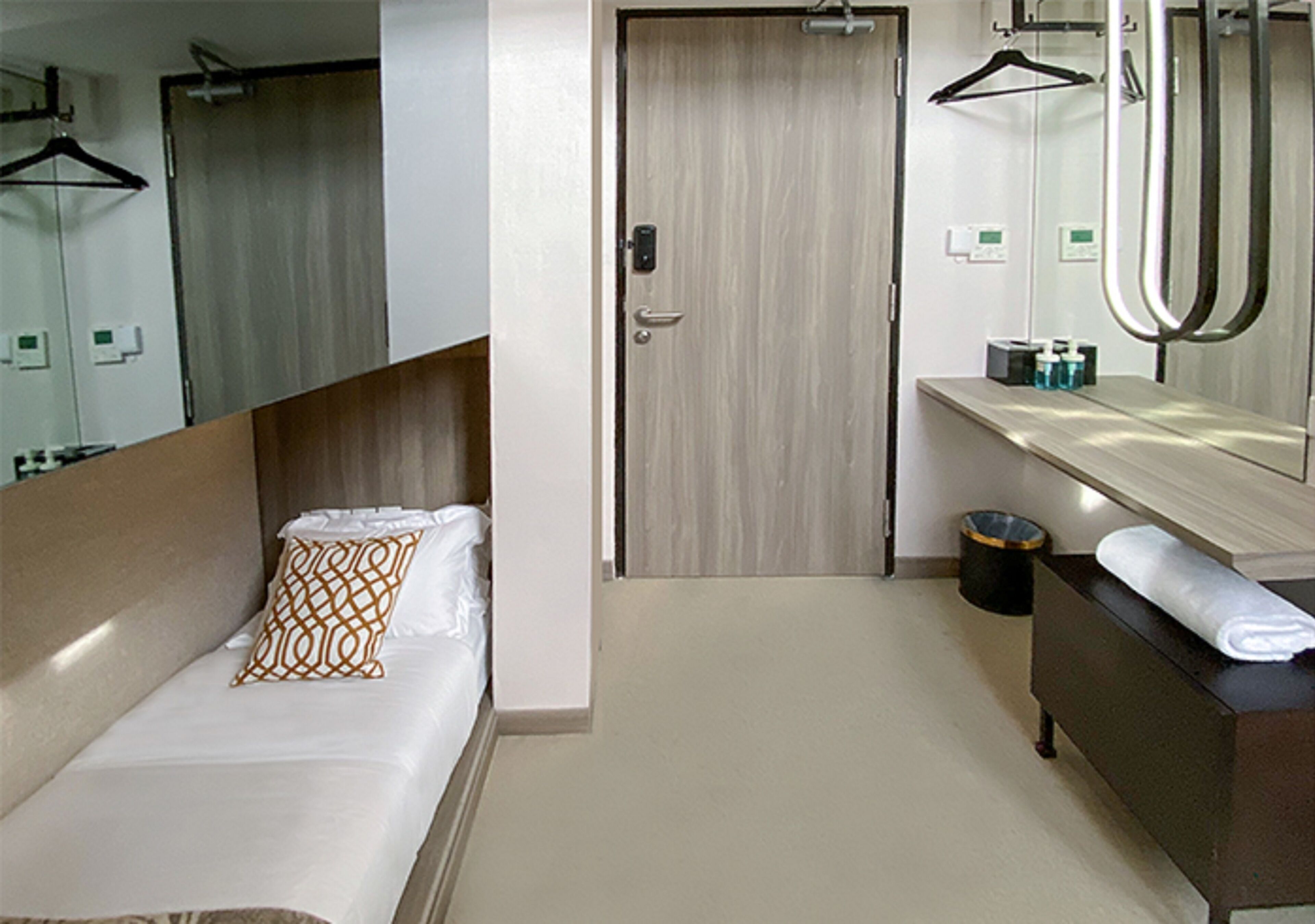 Een hotelkamer met een bed, een houten deur, een badkamer met een spiegel en een handdoek ernaast.