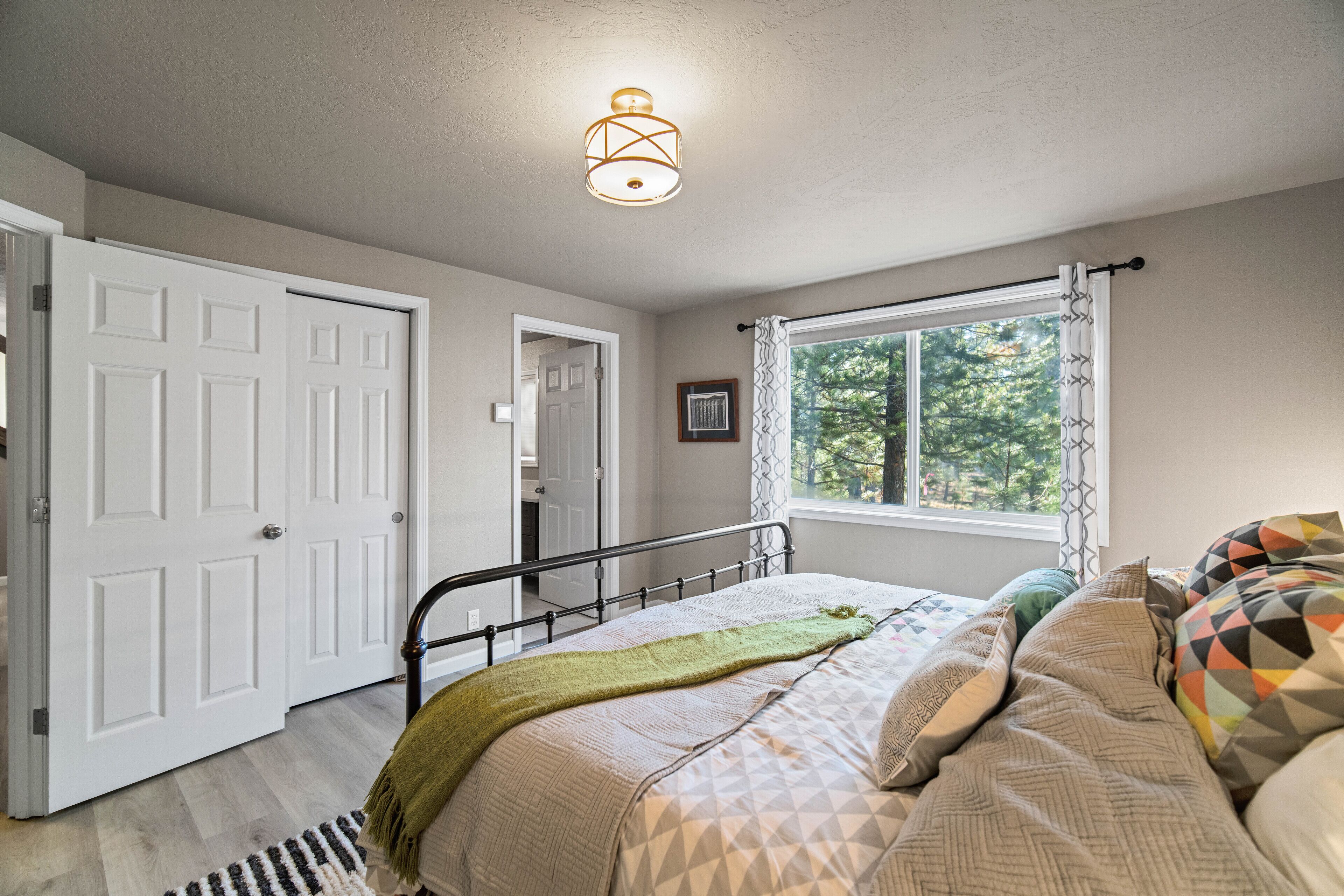 A bedroom with a bed, a window with curtains, a door, and a light fixture.