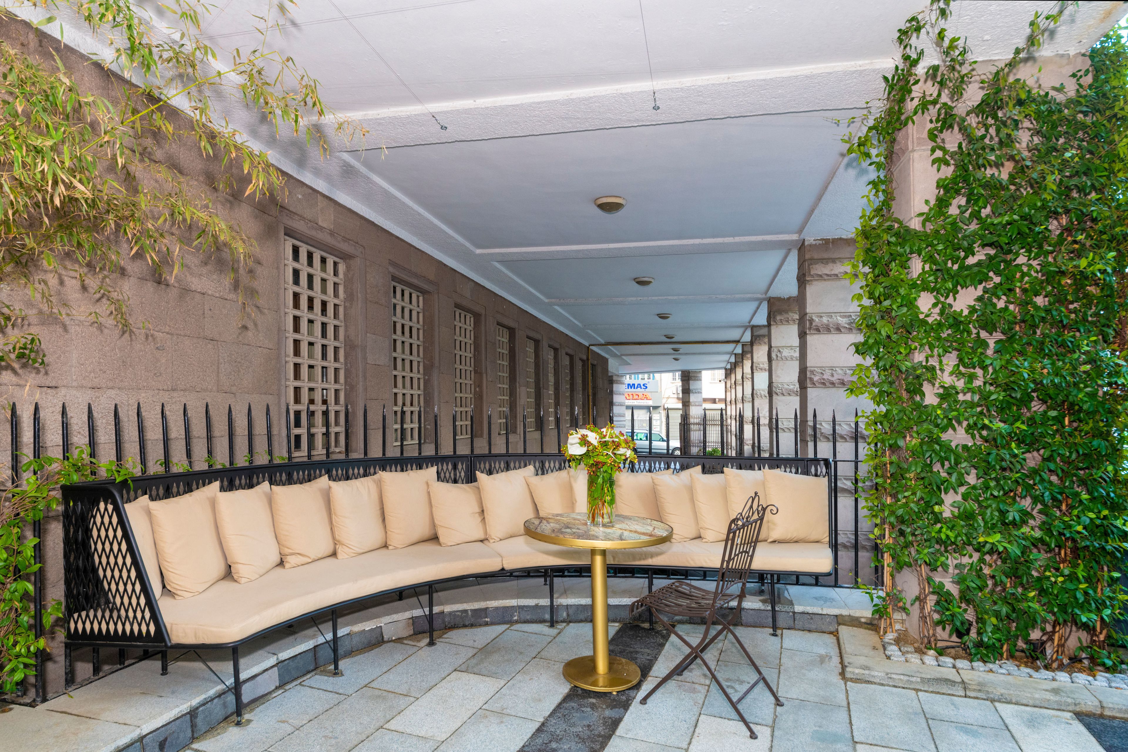 A curved sofa with beige cushions, a round table with a gold base, and a chair with a metal frame.