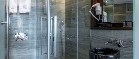Une salle de bain moderne dotée d’une douche à parois de verre, de toilettes, d’un meuble-lavabo avec un évier en marbre noir et d’un miroir au-dessus de l’évier.