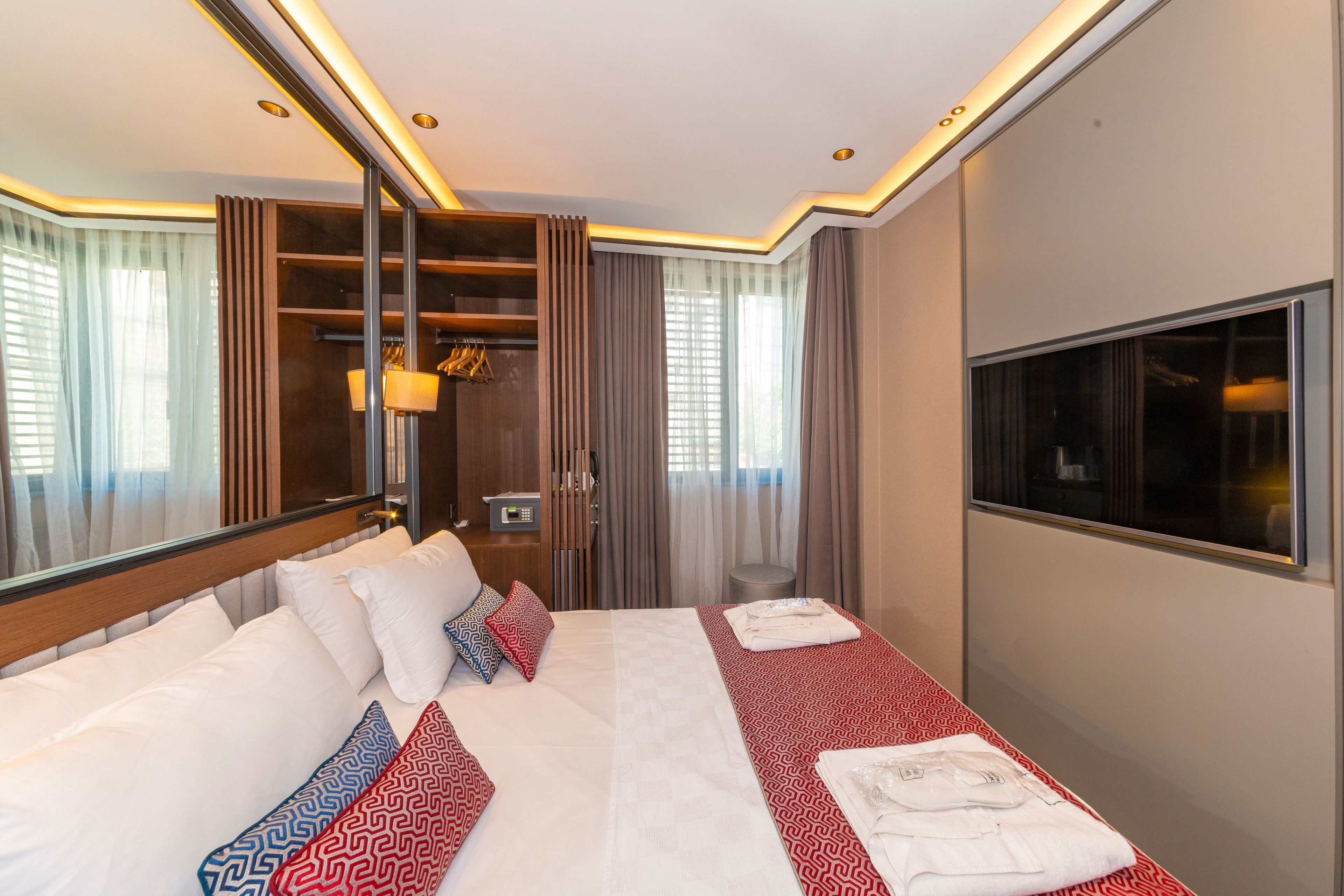 A hotel room with a large bed, a wardrobe, a vanity with a mirror, and a TV on the wall.