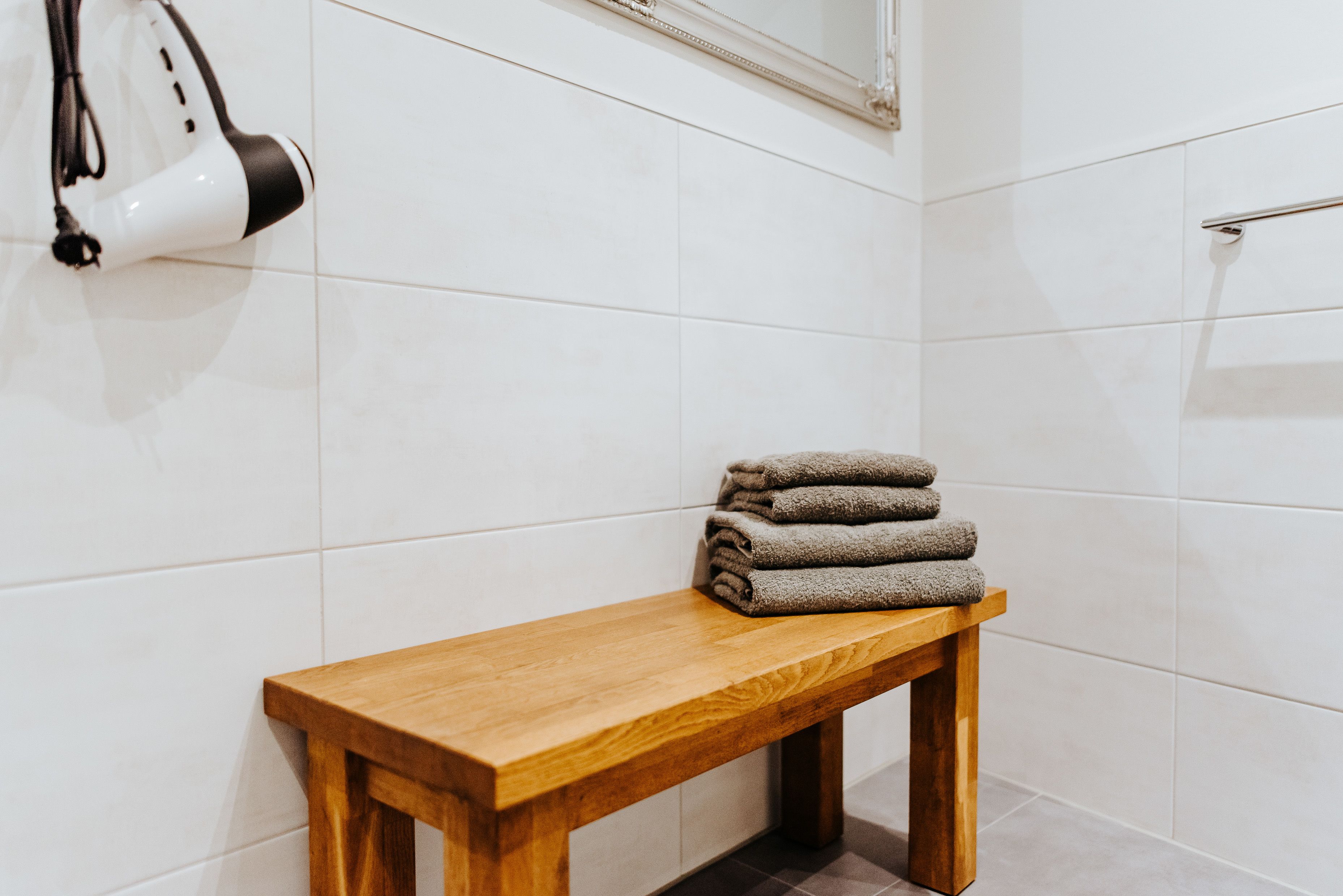 Un baño con baldosas blancas, un banco de madera y una pila de toallas.