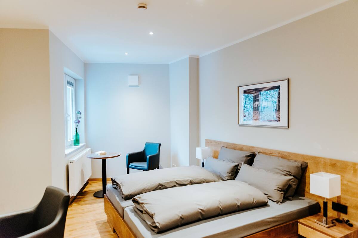 Ein modernes Hotelzimmer mit einem Bett, einem Sessel, einem kleinen Tisch und einem Fenster.