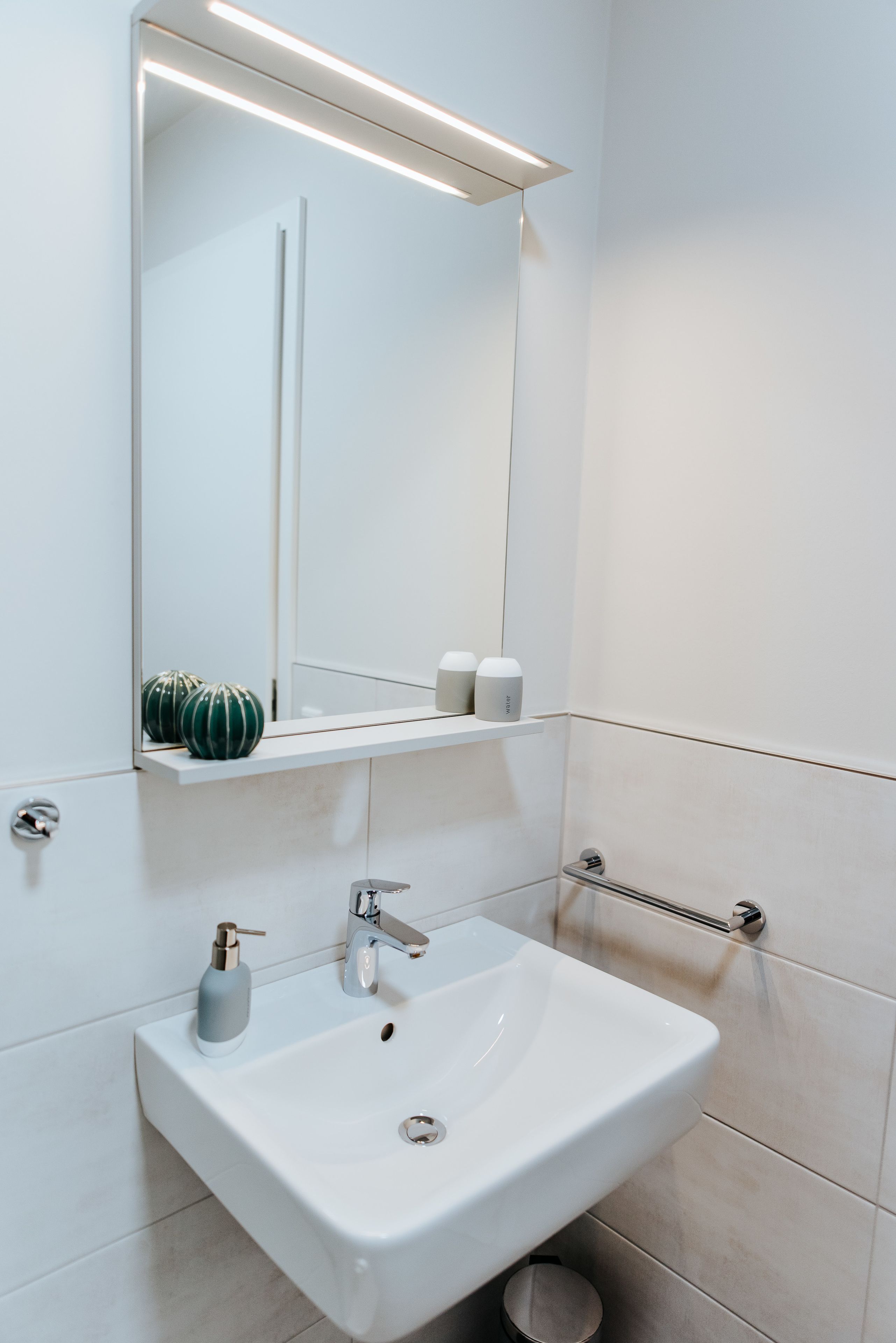 Een moderne badkamer met een wit wastafel, een spiegel en een plank met toiletartikelen.