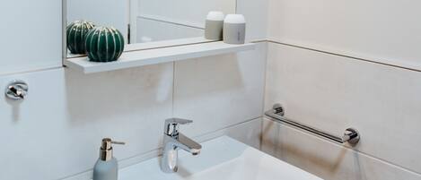 A modern bathroom with a white sink, a mirror, and a shelf with toiletries.