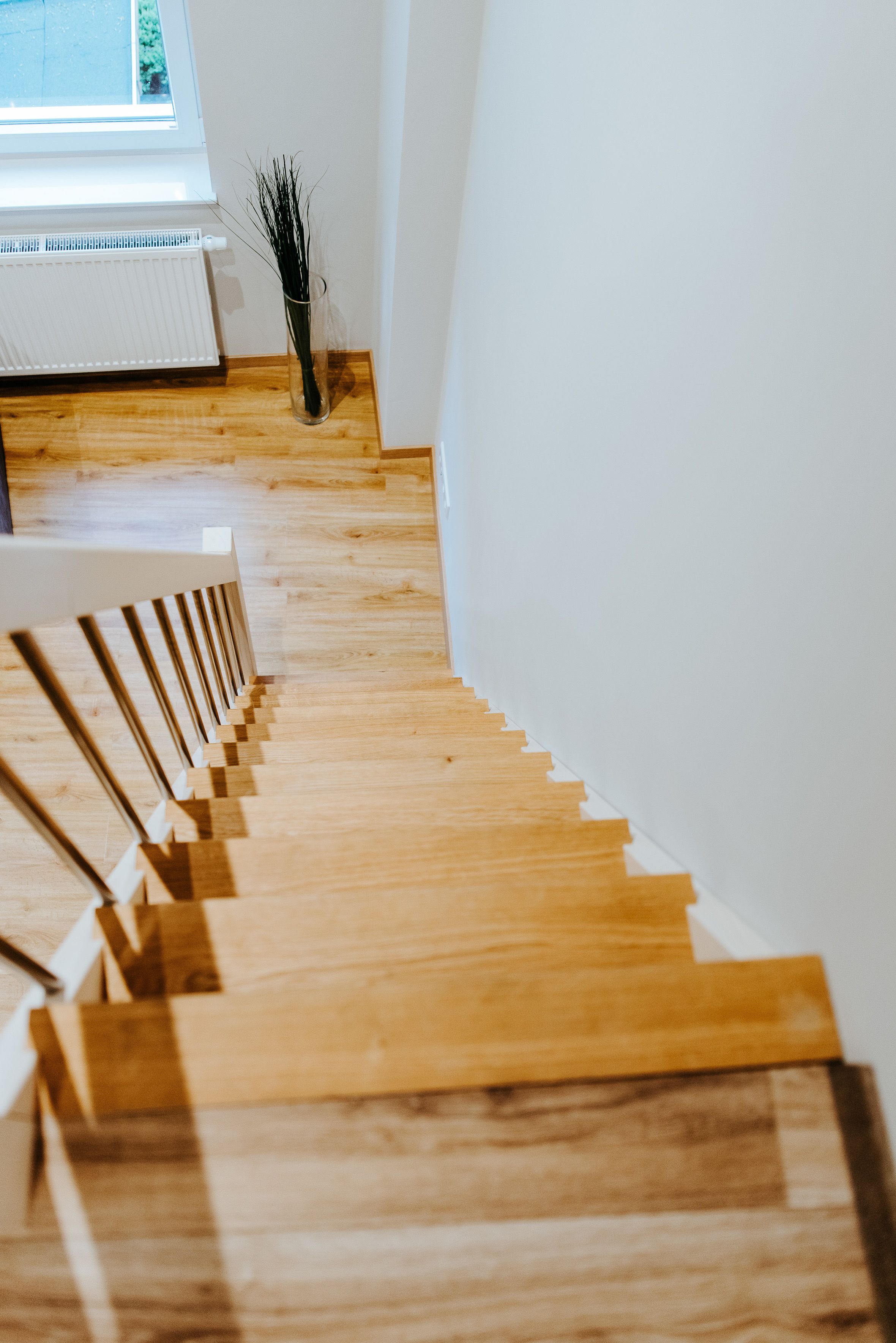 A wooden staircase with a white railing, leading to a window with a view of greenery outside.